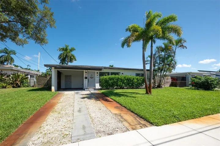 Single-story residence featuring a covered carport, concrete driveway, mature palm trees, and established landscaping