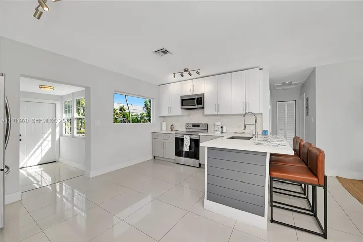 Kitchen featuring white cabinetry, stainless steel appliances, a central island with a grey paneled base, quartz countertops, and neutral tile flooring