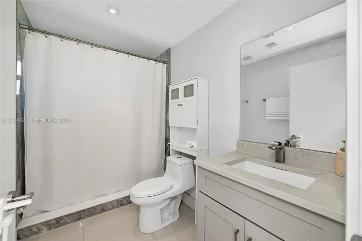 Bathroom featuring a stone-surface vanity with an integrated rectangular sink, wall-spanning mirror, one-piece toilet, and tile shower surround