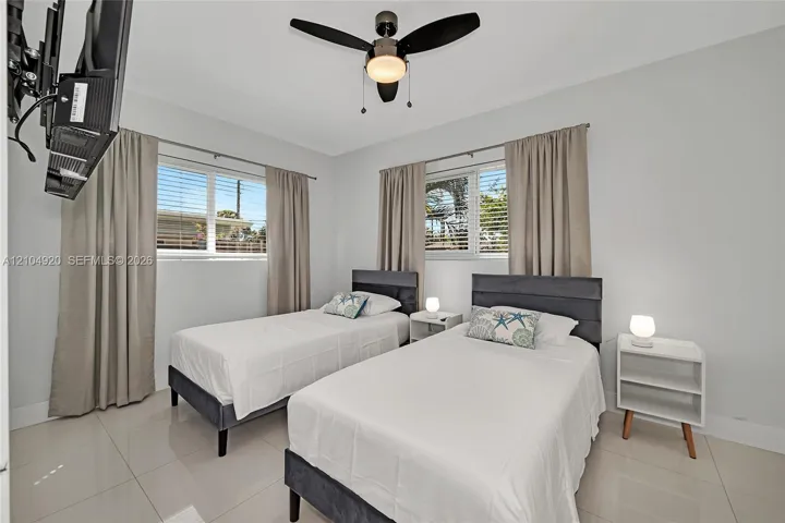 Neutral-toned interior space featuring light-colored tile flooring, multiple windows with horizontal blinds, and a contemporary ceiling fan with integrated lighting