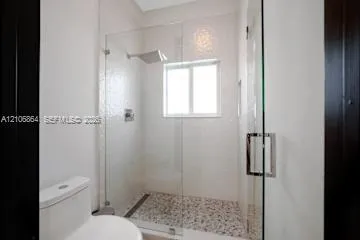 Walk-in shower with frameless glass enclosure, rainfall showerhead, mosaic stone flooring, and white tile surround