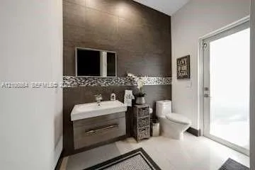 Wall-mounted floating vanity with integrated rectangular sink and wood-finish cabinetry, accented by floor-to-ceiling large-format wall tiling and a decorative glass mosaic tile border