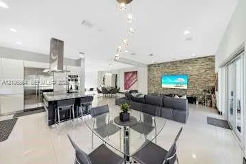 Open-concept living space featuring high-gloss cabinetry, stainless steel appliances, stone-veneer accent wall, and porcelain tile flooring