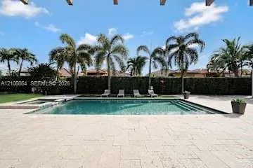 In-ground swimming pool with an integrated spa, surrounded by expansive stone paver hardscaping and mature palm trees