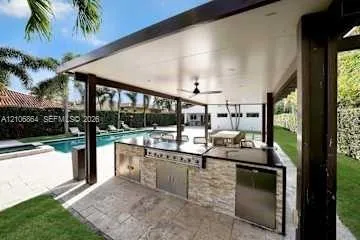 Covered outdoor kitchen featuring stone veneer cabinetry, stainless steel appliances, a flush-mount ceiling fan, and recessed lighting, situated by a swimming pool with stone paver decking