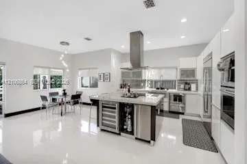 Contemporary kitchen featuring high-gloss cabinetry, a central island with integrated wine storage, a stainless steel chimney-style range hood, polished tile flooring, and built-in stainless steel double ovens