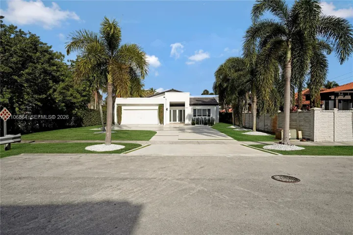 Modern architectural exterior featuring a concrete driveway, two-car garage, manicured lawn, and established palm trees