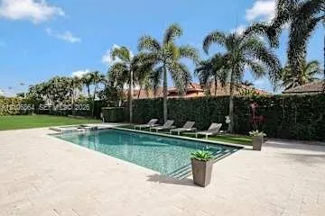 Rectangular swimming pool featuring stone paver decking, established palm trees, and a high perimeter hedge