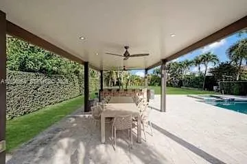 Covered patio featuring recessed lighting, a ceiling fan, an outdoor kitchen with stone veneer base, and a stone-paver deck overlooking a pool