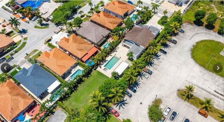 Aerial perspective of a multi-residence property featuring tiled roofing, rectangular in-ground swimming pools, paved exterior hardscaping, and mature palm landscaping
