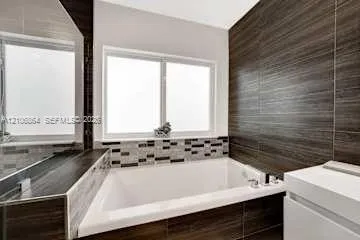 Built-in soaking tub with horizontal wood-finish tile surround, decorative stone-mosaic backsplash, and polished chrome faucet hardware