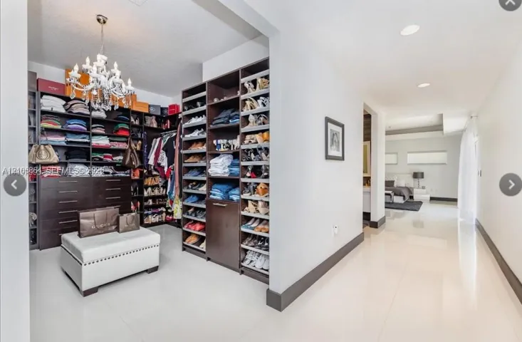 Custom dressing area featuring dark wood-finish built-in cabinetry, floor-to-ceiling shelving, drawers, and a ceiling-mounted crystal chandelier, complemented by polished tile flooring