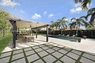 Outdoor living area featuring a covered pergola, concrete paver patio with grass joints, rectangular swimming pool, and privacy hedges