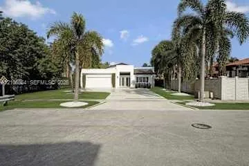 Single-story exterior featuring a concrete driveway, two-car garage, manicured lawn, and mature palm trees