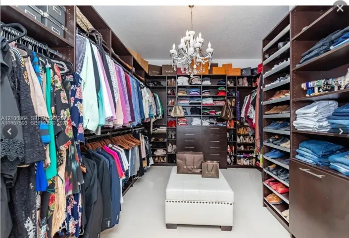 Walk-in closet featuring floor-to-ceiling built-in dark wood cabinetry, extensive shelving, integrated drawer storage, and a central chandelier fixture