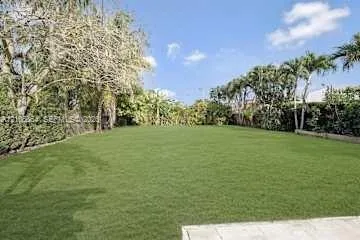 Expansive rear grounds featuring a manicured lawn, established perimeter hedges, and mature palm trees