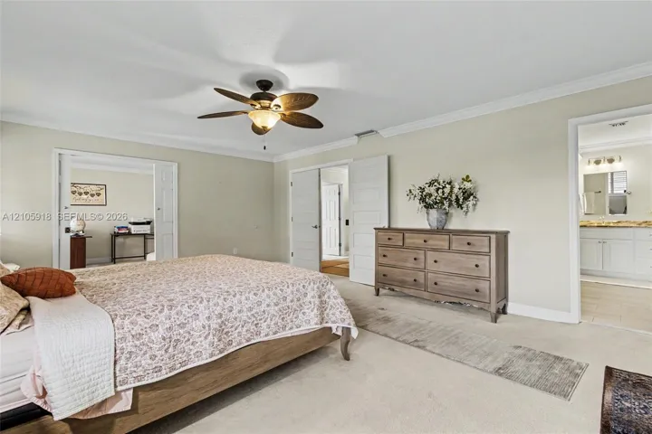 Neutral-toned room featuring a ceiling fan with integrated lighting, crown molding, and double-door entry