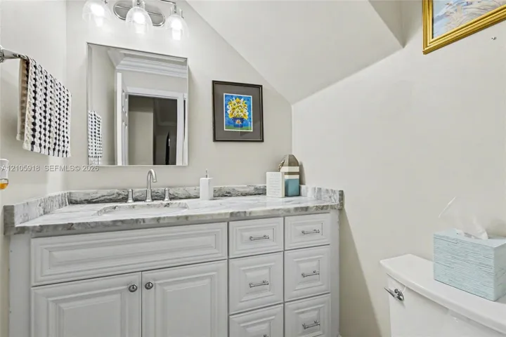 Bathroom vanity featuring white cabinetry, stone-patterned countertop, integrated sink, polished metal faucet, and wall-mounted three-light fixture