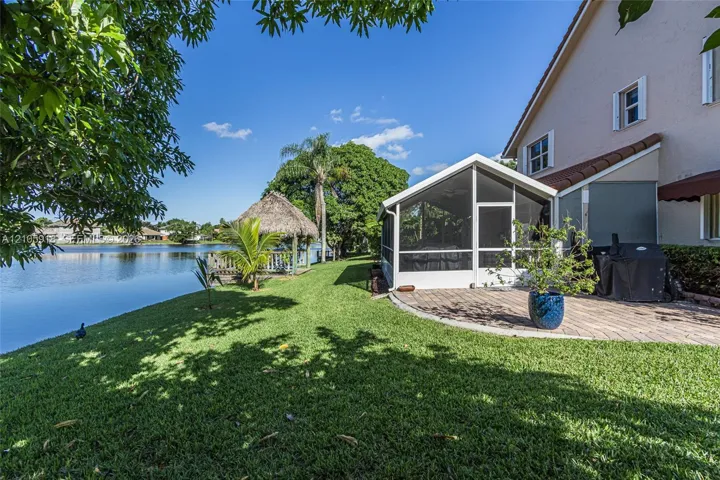 Waterfront backyard featuring a screened-in patio, paver terrace, and a thatched-roof gazebo