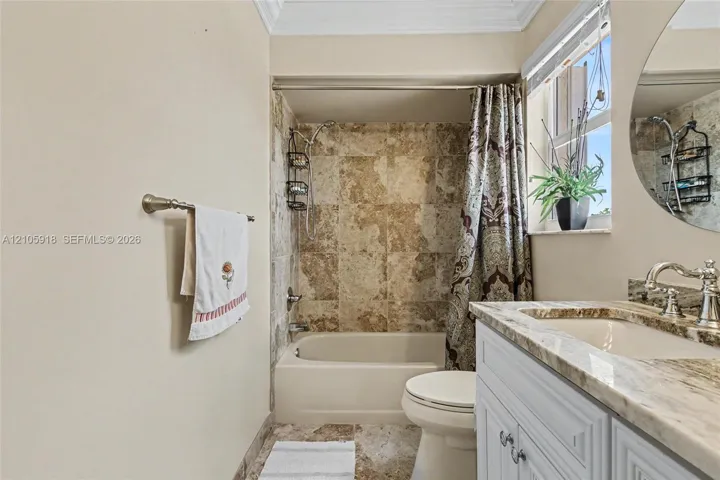 Bathroom featuring a tub-shower combination with natural stone surround, vanity with stone countertop and undermount sink, and circular wall-mounted mirror