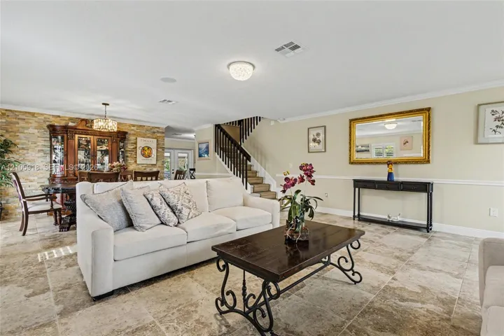 Open-concept interior featuring large-format stone tile flooring, a floor-to-ceiling textured stone accent wall, chair rail molding, and a staircase with decorative wrought iron railing