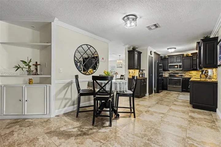 Kitchen featuring dark cabinetry, stone-finish countertops, ceramic tile flooring, and built-in shelving with crown molding