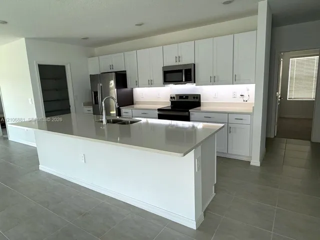 Kitchen featuring white shaker-style cabinetry, a large island with a composite countertop, under-cabinet lighting, stainless steel appliances, and tile flooring