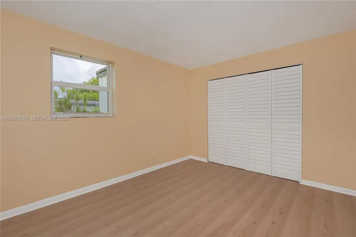 Room interior featuring wood-finish flooring, a single-hung window, and white louvered bifold closet doors