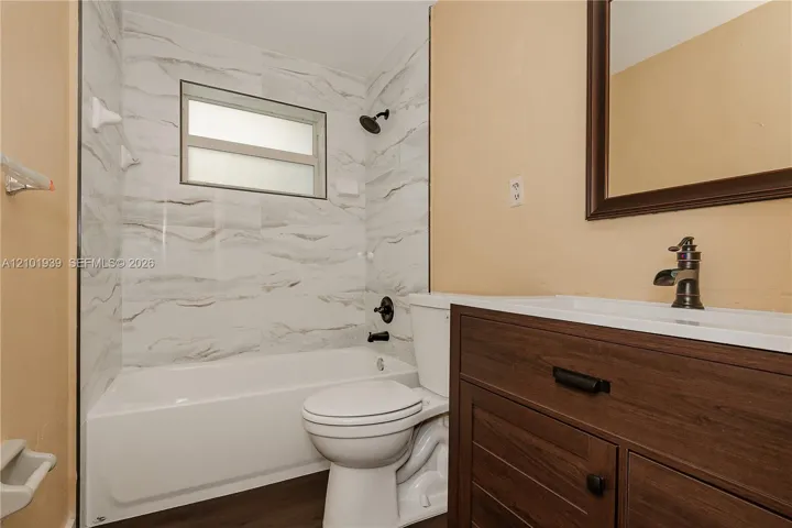 Bathroom featuring a wood-finish vanity with a rectangular sink, patterned tile shower surround, matte black fixtures, and a recessed window