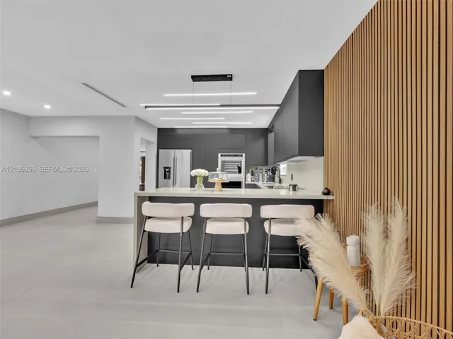 Kitchen featuring matte dark cabinetry, a waterfall-edge island with stone-finish countertop, linear LED pendant lighting, and a floor-to-ceiling wood slat accent wall