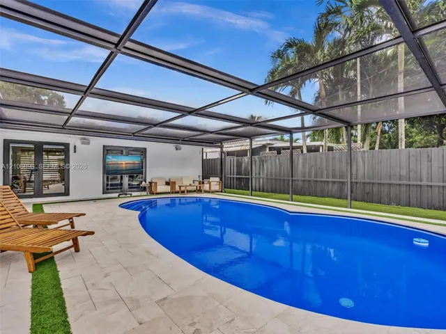 Screened pool enclosure featuring a custom-shaped swimming pool, light-toned stone pool deck with integrated turf detailing, and a high-privacy wood fence