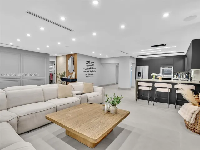 Open-concept interior featuring recessed ceiling lighting, matte black flat-panel cabinetry, a stone-topped kitchen island, neutral large-format flooring, and decorative wall molding