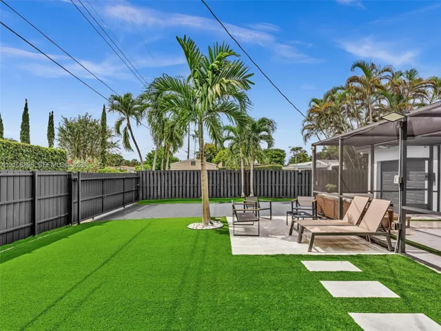 Backyard featuring synthetic turf, a stone paver patio, a screened enclosure, and privacy fencing