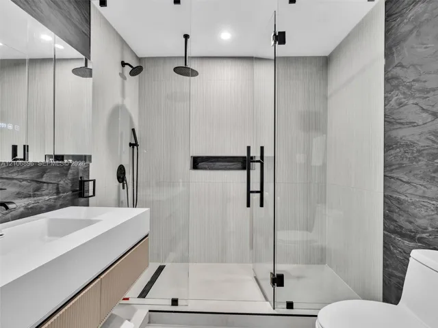 Bathroom featuring a floating vanity with integrated sink, walk-in shower with frameless glass enclosure, dual shower heads including a ceiling-mounted rainfall fixture, and recessed wall niche