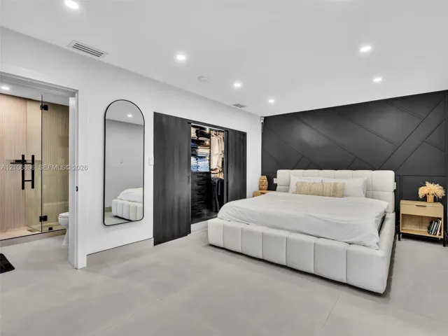 Bedroom featuring large-format tile flooring, a geometric paneled accent wall, sliding dark-finish wardrobe doors, and recessed ceiling lighting