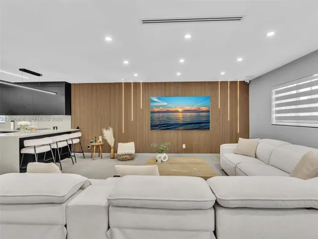 Slatted wood-finish feature wall with integrated vertical lighting, recessed ceiling lighting, linear kitchen island with stone-finish countertop, matte black linear pendant light, and horizontal blinds