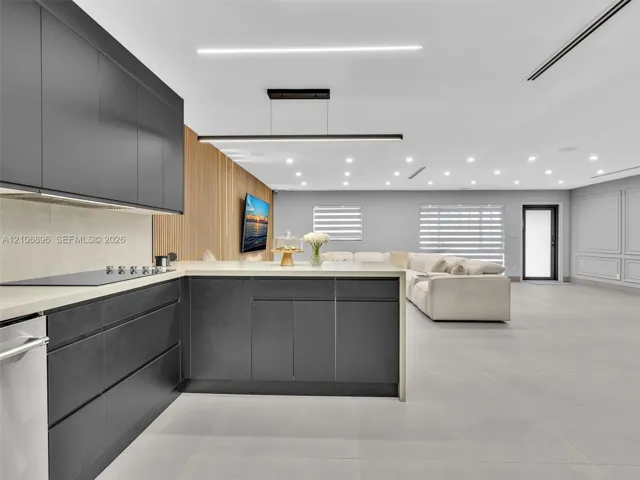Contemporary kitchen featuring flat-panel charcoal cabinetry, light-toned stone countertops, linear pendant lighting, wood-slat accent wall detailing, and large-format tile flooring