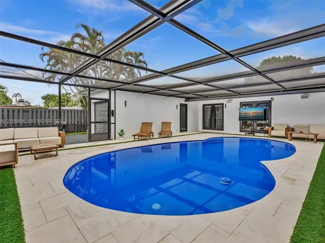 Screen-enclosed pool area with stone tile decking, synthetic turf accents, and perimeter fencing