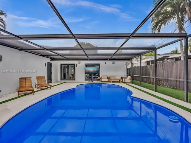 Screen-enclosed pool area featuring concrete decking, synthetic turf accents, and dual sets of French doors