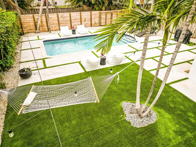 Backyard featuring an inground swimming pool, concrete pavers with turf infill, synthetic turf lawn, mature palm trees, and wood-panel privacy fencing