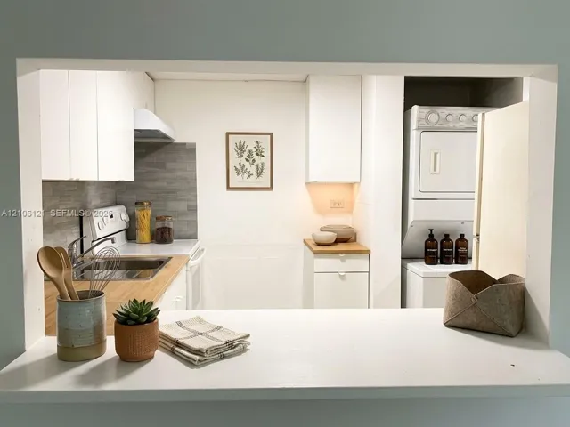 Kitchen featuring white cabinetry, wood-surface countertops, gray horizontal tile backsplash, and a stacked laundry unit