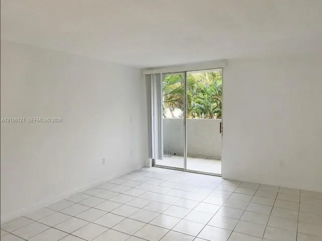 Interior space featuring light-colored tile flooring, vertical blinds, and a sliding glass door opening to a concrete balcony
