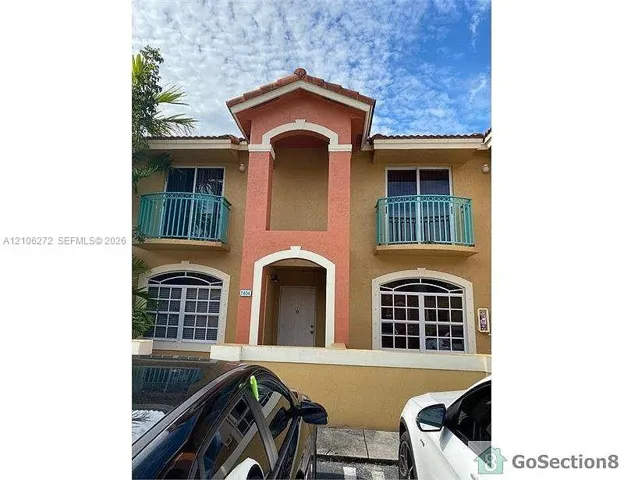 Two-story exterior featuring a tile roof, stucco finish, arched windows with decorative muntins, and dual metal-railed balconies