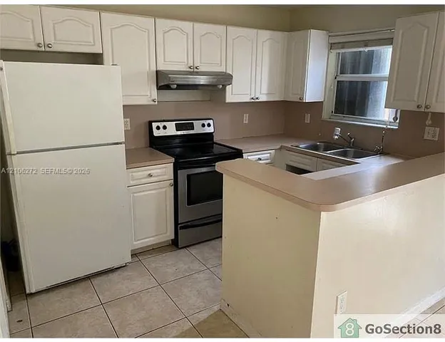 Kitchen featuring white shaker-style cabinetry, stainless steel range with overhead hood, dual-basin sink, laminate countertops, and ceramic tile flooring