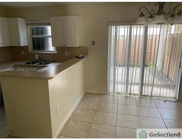 Kitchen featuring white cabinetry, a dual-basin sink, a raised breakfast bar, ceramic tile flooring, and a sliding glass door