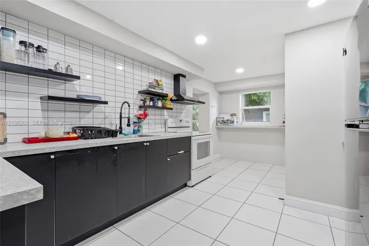 Kitchen featuring black flat-panel cabinetry, light-toned countertops, white subway tile backsplash, floating shelving, and white tile flooring
