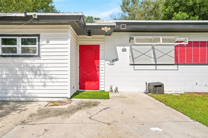 Exterior facade featuring horizontal siding, a covered entryway with a red paneled door, concrete driveway, and window awnings