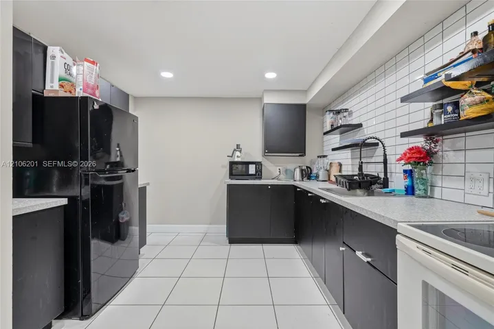 Kitchen featuring matte black flat-panel cabinetry, light-toned countertops, white subway tile backsplash, recessed ceiling lighting, and tile flooring