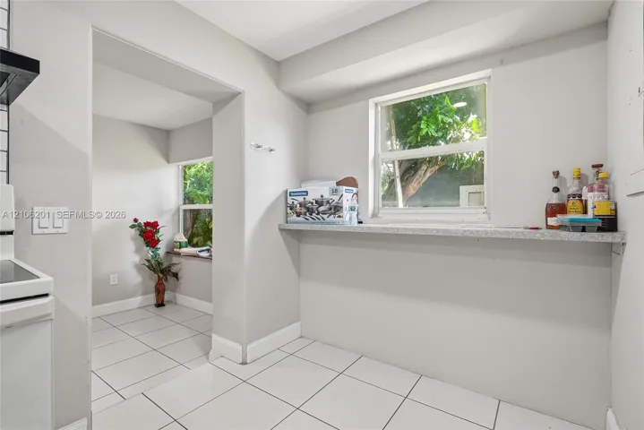 Kitchen area featuring white ceramic tile flooring, light-toned walls, and a built-in stone-finish ledge under a window