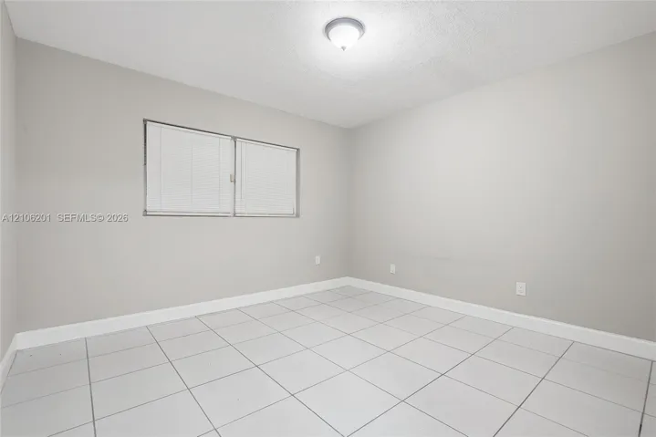 Neutral-toned interior room featuring large-format ceramic tile flooring, a dual-pane horizontal sliding window, and a ceiling-mounted flush light fixture